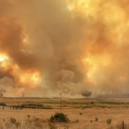 An image of the Slink wildfire showing flames and smoke rising over a field.