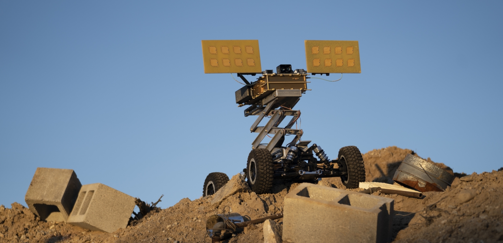 A photo of a small unmanned vehicle with solar panels on top, on top of a mound of dirt.
